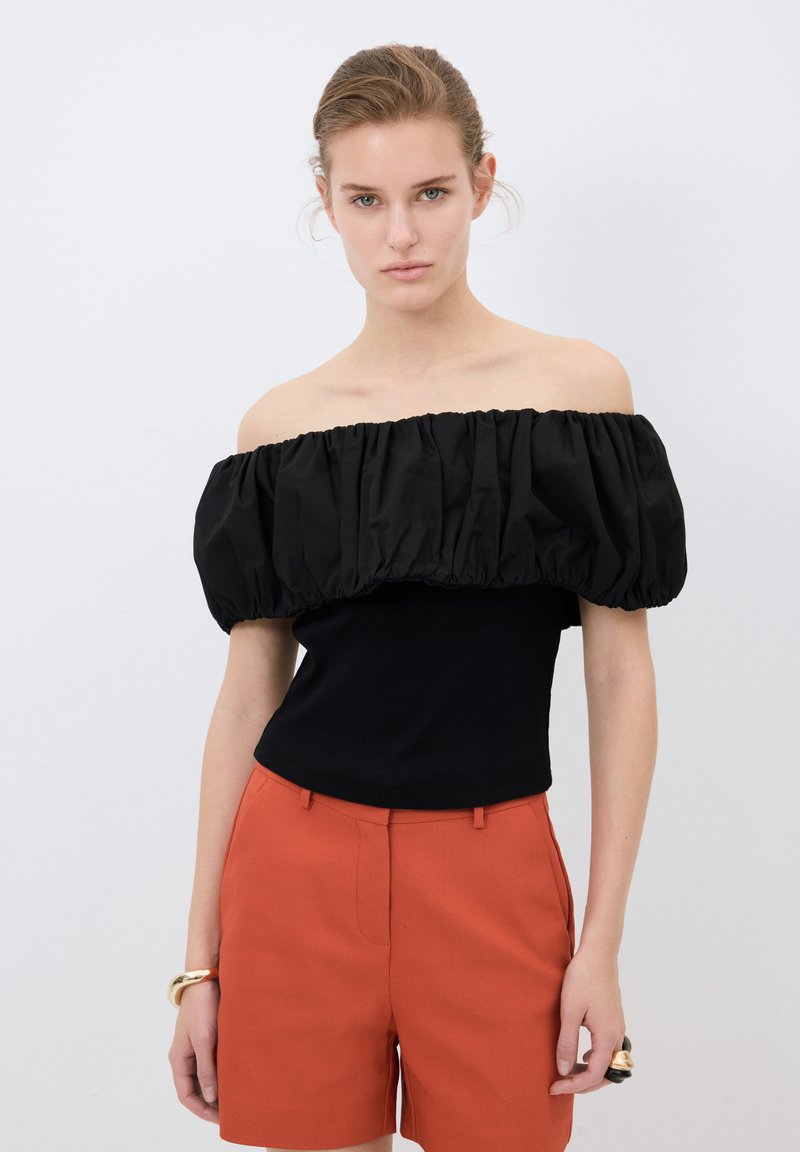 Top nero off-the-shoulder con maniche a sbuffo arricciate, abbinato a pantaloni corti arancioni. Tessuto liscio con design strutturato.