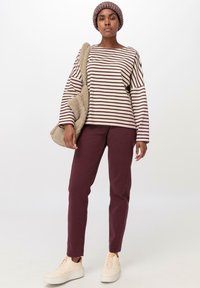 Gestreiftes Langarmoberteil in Creme und Bordeaux, kombiniert mit bordeauxfarbenen Hosen. Eine strukturierte beigefarbene Tasche und hellfarbige Sneakers runden das Outfit ab.
