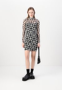 Mekko, jossa on pitkät hihat ja joka sopii vartalon myötäisesti, valmistettu läpinäkyvästä kankaasta ja jossa on kukkakuosi mustalla, harmaalla ja vaimealla vaaleanpunaisella. Yhdistettynä tukevien mustien kenkien kanssa.