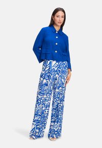Cropped blue linen jacket with rounded collar and large buttons, paired with wide-leg trousers featuring a bold blue and white abstract pattern.