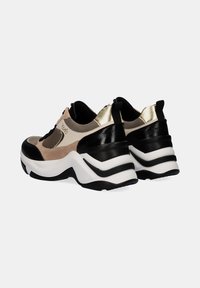 Zapatillas deportivas voluminosas que combinan gamuza beige, cuero negro liso y detalles dorados. Suela intermedia blanca gruesa con detalles en negro.