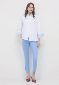 Weißes Hemd mit gestreiften blauen Manschetten, kombiniert mit hellblauen Hosen und burgunderfarbenen High Heels. Hat einen lockeren Schnitt und eine Knopfverschlusst.