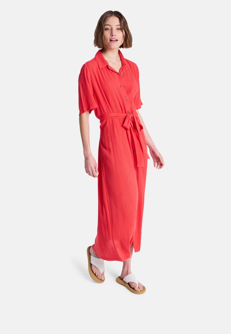 Koralfarvet maxikjole med korte ærmer, knaplukning foran og bindebånd i taljen. Fremstillet af letvægtsstof, har en flydende silhuet og afslappet pasform.