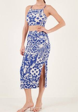 Vrouw draagt een tweedelig outfit met blauw-wit patroon, bestaande uit een cropped top en een hooggesneden rok met een zijslit, gecombineerd met beige sandalen met hak.