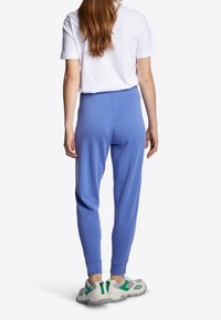 Pantalones de chándal azul con puños acanalados y cinturilla elástica, combinados con camiseta blanca y zapatillas multicolores con acentos verdes.