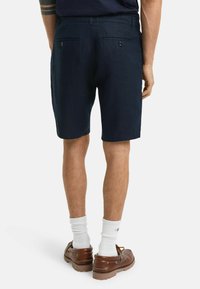 Marineblauwe shorts van lichte stof, met een rechte snit, twee achterzakken met knopen en een zachte textuur.