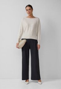 Lichtbeige trui met een geribde rand, gecombineerd met donker gestreepte wijde broek. De look wordt compleet gemaakt met een crèmekleurige handtas met een gouden ketting.