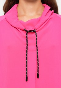 Fuchsia sweatshirt met een col, afgewerkt met een zwart-wit trekkoord met plastic uiteinden. Glad materiaal en een ontspannen pasvorm.