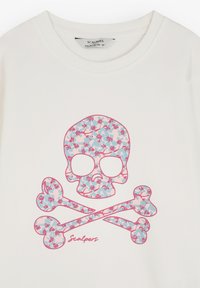 Sudadera blanca con un gráfico de calavera y huesos cruzados florales en rosa y azul claro. Nombre de la marca "Scalpers" impreso debajo del diseño.
