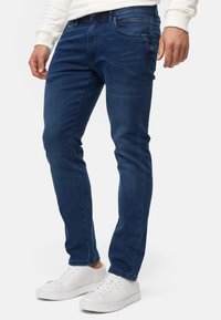 Blå denimjeans med smal passform, med frontlommer og knappestolpe. Brukt sammen med hvite joggesko, som fremhever en avslappet stil.