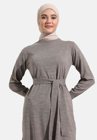 Long-sleeved grey dress made of knit fabric, featuring a waist tie for adjustment. A matching hijab completes the outfit, highlighting simplicity.