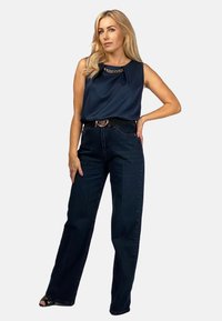 Granatowa bezrękawnik z detalami w postaci łańcuszka, w połączeniu z ciemnoniebieskimi jeansami o wysokim stanie. Czarbelts i obuwie na obcasie dopełniają stylizację.