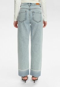 Jeans de tiro alto en azul claro con un corte de pierna ancha, con dobladillo deshecho y dos bolsillos traseros. Hechos de denim con una textura suave.