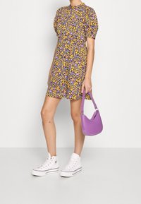 Blommig klänning med puffärmar i lila, gult och lavendel, tillsammans med vita högstövlar och en liten lavendelfärgad axelväska.