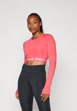 Top corto rojo de manga larga, con un logotipo blanco "NIKE PRO" en el dobladillo, combinado con leggings negros de cintura alta. Textura suave.