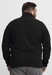Svart fleecejakke med høy krage, lange ermer og myk tekstur. Har en rett passform og minimale designdetaljer.