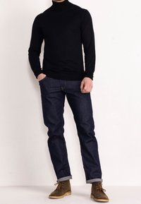 Schwarzer Rollkragenpullover kombiniert mit dunkelblauen Jeans in geradem Schnitt sowie braunen Wildlederstiefeln mit Schnürung und Kreppsohle.