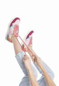 Zapatillas coloridas con parte superior rosa y acentos en púrpura, turquesa y marrón, paneles texturizados y cordones rosas. Piernas en posición elevada.