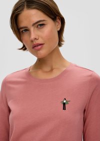 Różowa, długosleevowa koszulka wykonana z miękkiej bawełny, z małą haftowaną grafiką osoby w zielonym i czarnym ubraniu na piersi.