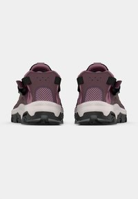 Ζευγάρι μοβ και ροζ παπούτσια πεζοπορίας με μαύρες σόλες, φαίνονται από πίσω σε λευκό φόντο.