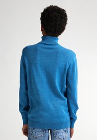 Hochwertiger Rollkragenpullover in hellem Blau, weicher Stoff, gerippter Kragen und Bündchen, lockere Passform, getragen mit hellblauen Jeans, Rückansicht.