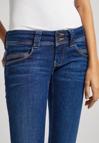 Dark blue denim jeans with a fitted design, featuring a button and zipper closure, front pockets, and yellow stitching accents.