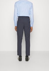 Navy checkered trousers in a tailored fit, made from lightweight fabric. Features side pockets and cuffed hems. Worn with a light blue shirt.