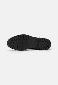 Semelle en caoutchouc noir avec un motif de traction texturé et un logo. Design durable, adapté à l'adhérence et au confort dans diverses conditions.