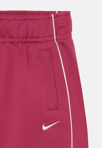 Nike sporta bikses spilgtā rozā krāsā ar baltām apmalēm. Iespējas ietver elastīgu jostu un sānu kabatu. Mīksta faktūra.