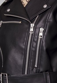 Czarna skórzana kurtka motocyklowa z metalowymi zamkami błyskawicznymi, epoletami i teksturowanym wykończeniem. Posiada pasek w talii oraz kilka kieszeni zapinanych na zamek.