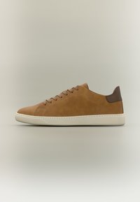 Baskets basses en cuir marron avec des lacets et une semelle beiges, dotées d'une languette de talon marron foncé, sur un fond neutre.