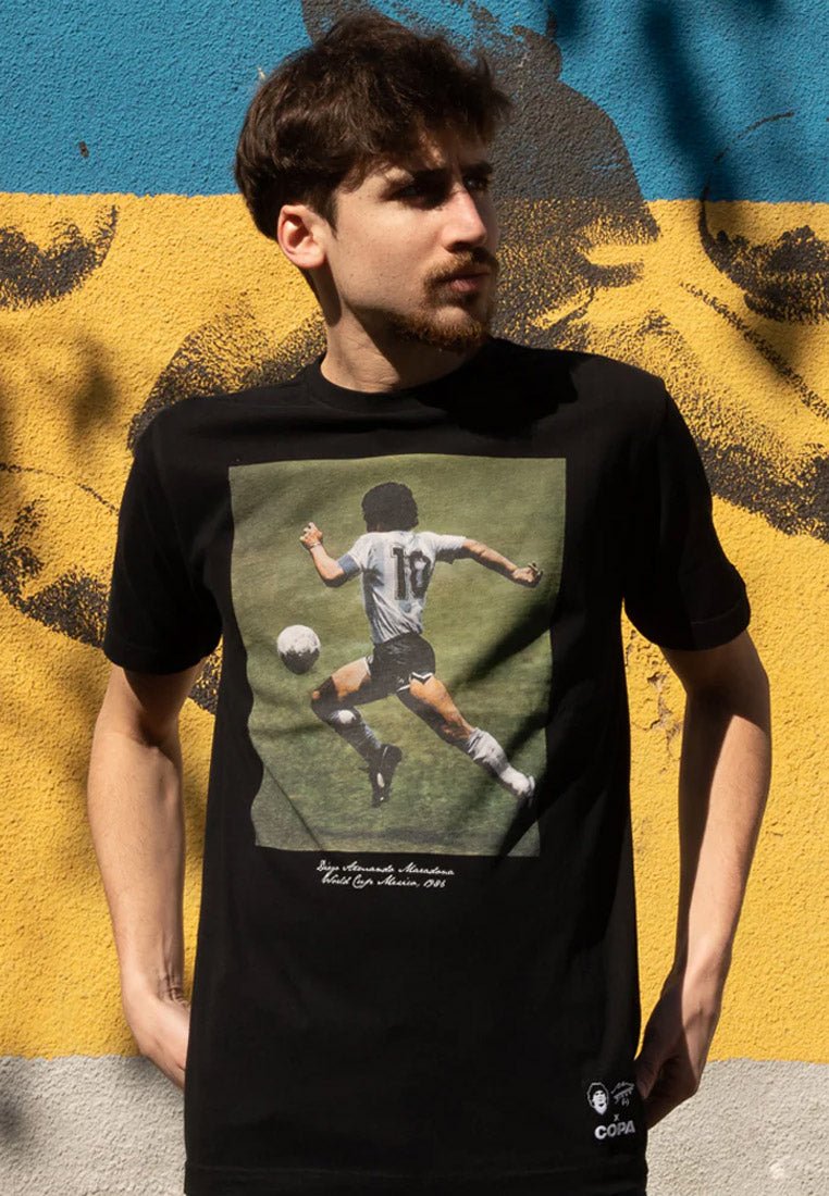 Sort t-shirt med grafisk tryk af en fodboldspiller i aktion, med detaljeret tekst under billedet. Blødt bomuldsstof.