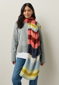 Bufanda a rayas multicolores con una tela ligera y texturizada. Presenta tonos de rojo, azul, amarillo y crema en diferentes anchos.