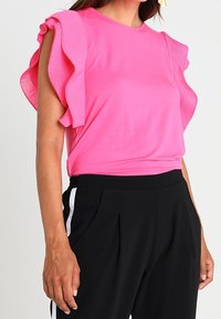 Top rosa de manga corta con detalles de volantes texturizados en los hombros, combinado con pantalones negros de tiro alto con franjas blancas en los laterales.