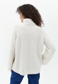Helles Cremefarbener Rollkragenpullover aus weichem Strickmaterial. Verfügt über einen gerippten Kragen und einen leicht übergroßen Schnitt mit strukturierter Oberfläche.