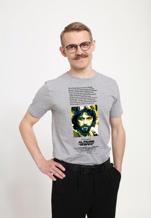 Grå bomulds t-shirt med et grafisk motiv af en mand med mørkt hår og blå accenter, samt tekst om filmen "Serpico" nedenunder.