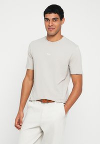 Jasnoszara bawełniana koszulka z krótkim rękawem, okrągłym dekoltem, z małym białym logo "BOSS" na piersi. Prosty design.