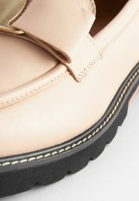 Light pink leather shoe with a rounded toe, featuring a wide strap and gold hardware. Black rubber sole with textured detailing.