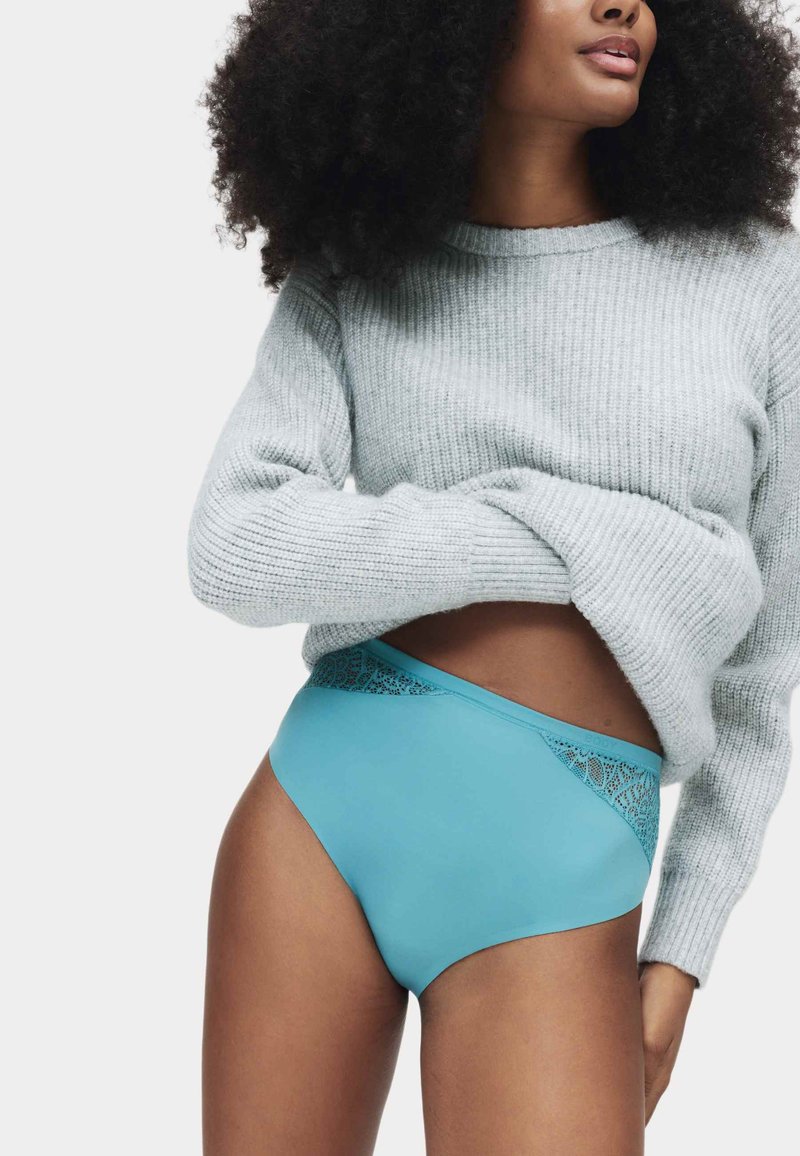 Hoge taille ondergoed in teal met kanten details aan de tailleband, gecombineerd met een lichtgrijze geribbelde trui. Zachte, rekbare stof.