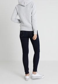 Sweatshirt à capuche gris associé à un jean skinny foncé et des baskets blanches, présentant un design ajusté et une texture lisse.