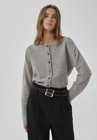 Grauer Wollcardigan mit Rundhalsausschnitt, Knopfleiste vorne und gerippten Bündchen, kombiniert mit hoch taillierter schwarzer Hose und einem Gürtel mit doppelter Schnalle.