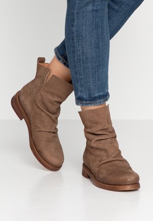 Bottines en daim marron avec petits talons en bois portées avec un jean bleu foncé raccourci sur fond blanc.