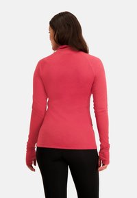 Langsleeve, strakke top in felroze, gemaakt van zacht materiaal. Bevat duimopeningen en een opstaande kraag voor een gestroomlijnde look.