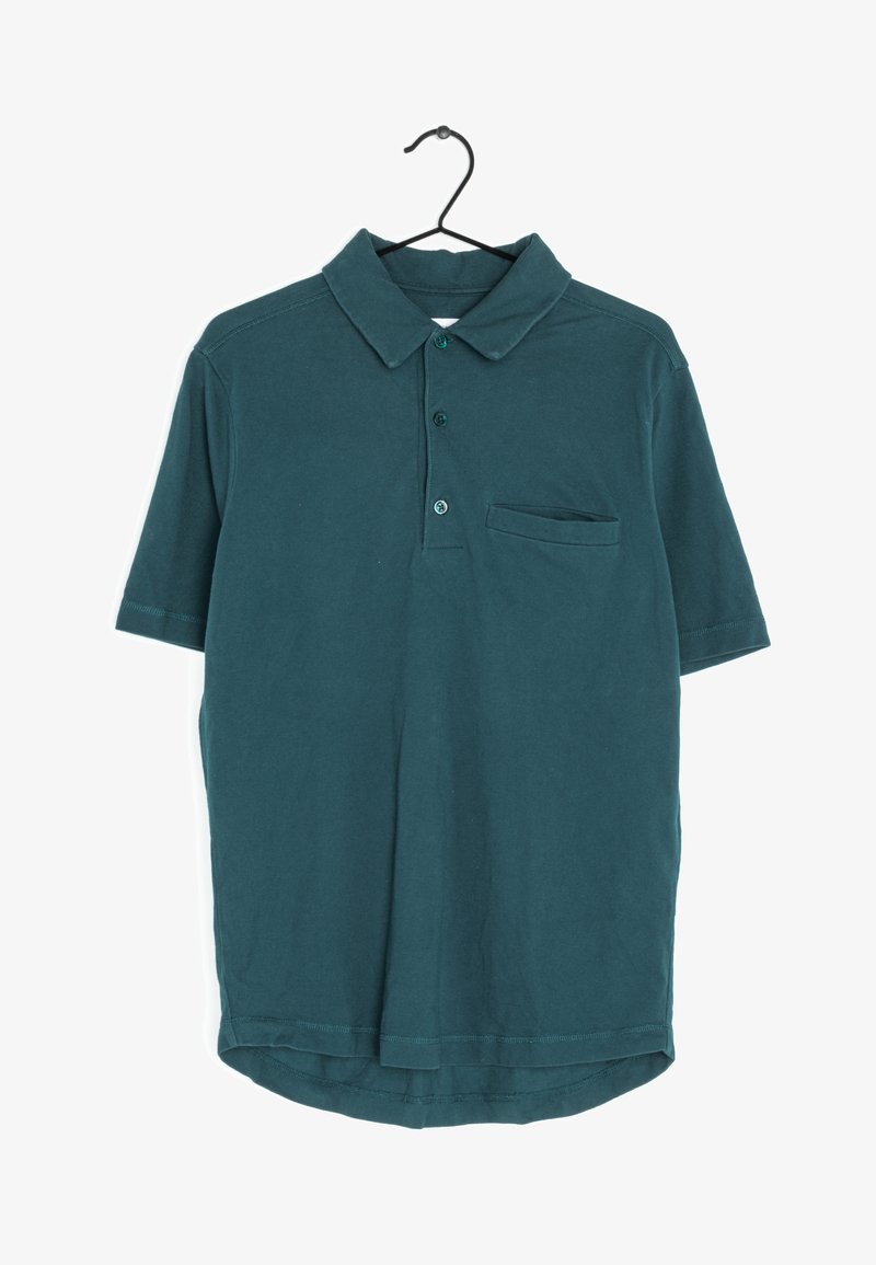Polo shirt court en teal foncé avec col, trois boutons et une petite poche poitrine suspendue à un cintre noir.