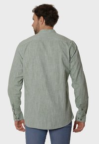 Camisa verde de manga larga con un patrón texturizado y tejido, y puños con botones. Tiene un cuello estándar y un dobladillo curvado.