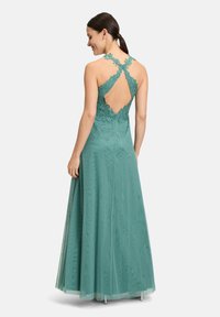 Turkusowa wieczorowa sukienka z koronkowymi detalami, krzyżującymi się ramiączkami i otwartym plecami. Długa spódnica wykonana z gładkiego, lekkiego materiału.