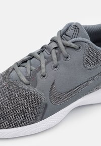 Harmaa urheilukenkä, jossa on verkkomainen ja synteettinen päällinen, ja jossa on kuvioitu harmaa kärkipala sekä Swoosh-logo, harmaat nauhat ja valkoinen pohja.