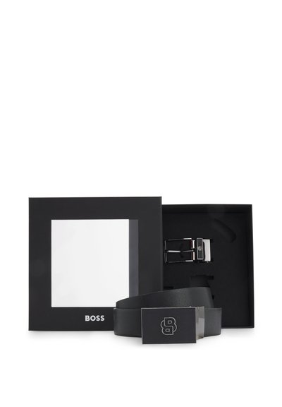 Ceinture en cuir noir avec une boucle argentée, ornée d'un logo. Emballée dans une boîte noire avec une fenêtre transparente.