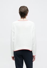 Λευκό πλεκτό πουλόβερ με φαρδιά λαιμόκοψη και κόκκινη διακοσμητική ραφή κατά μήκος του γιακά και του τελειώματος. Διαθέτει μακριά μανίκια και άνετη εφαρμογή.