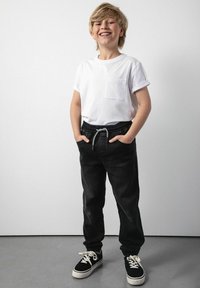 Biała bawełniana koszulka z kieszonką na piersi, w połączeniu z czarnymi dżinsowymi joggerami z elastycznym pasem i białym sznurkiem, oraz czarnymi sneakersami.